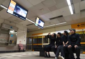 同學在捷運月台等候電視觀看自己的作品播出。